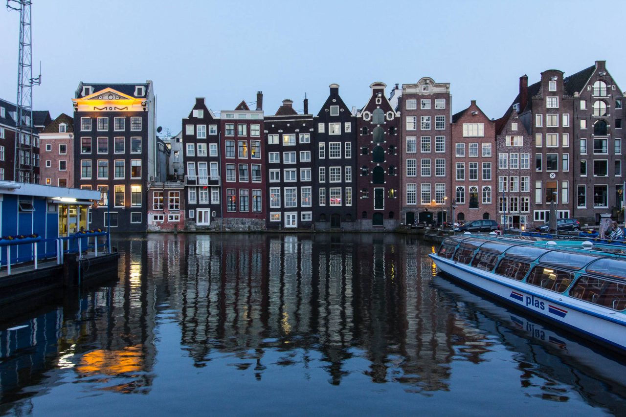 Lit canal houses reflected in the water at dusk with a boat moored in front