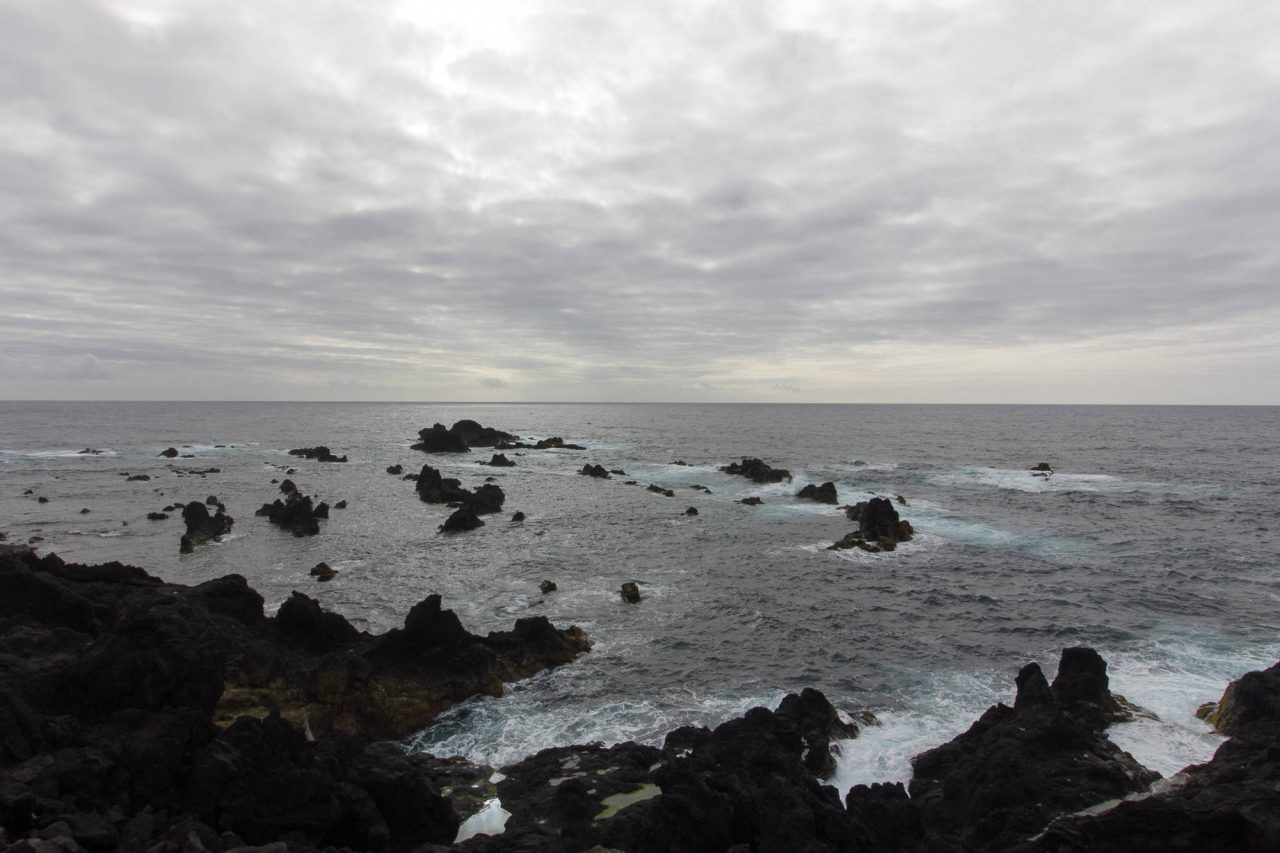 Long exposure of the sea washing over dark volcanic rocks under a grey sky