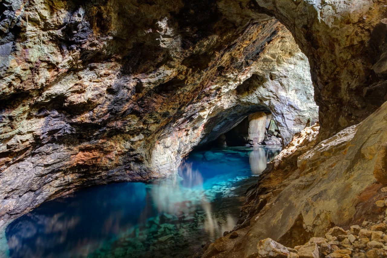 Inside a cave with an opening above and bright blue water below